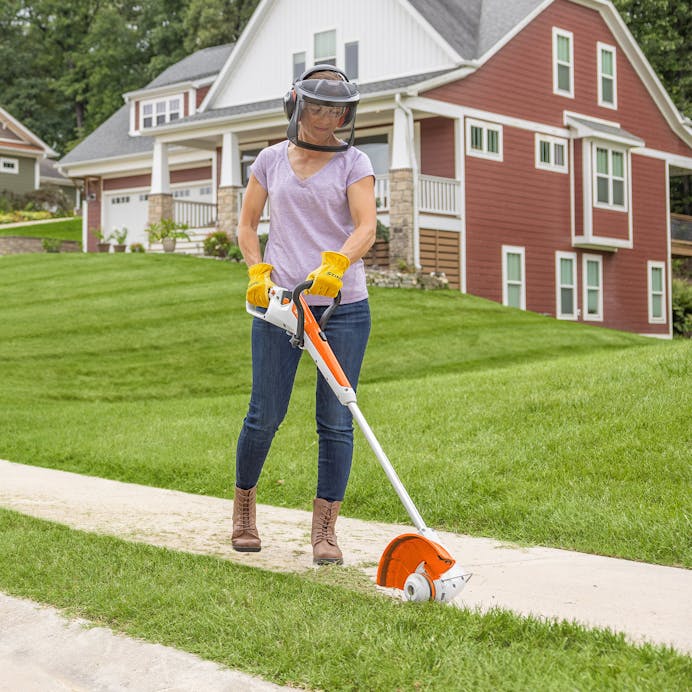 Woman with face guard using edger attachement on Stihl FSA30