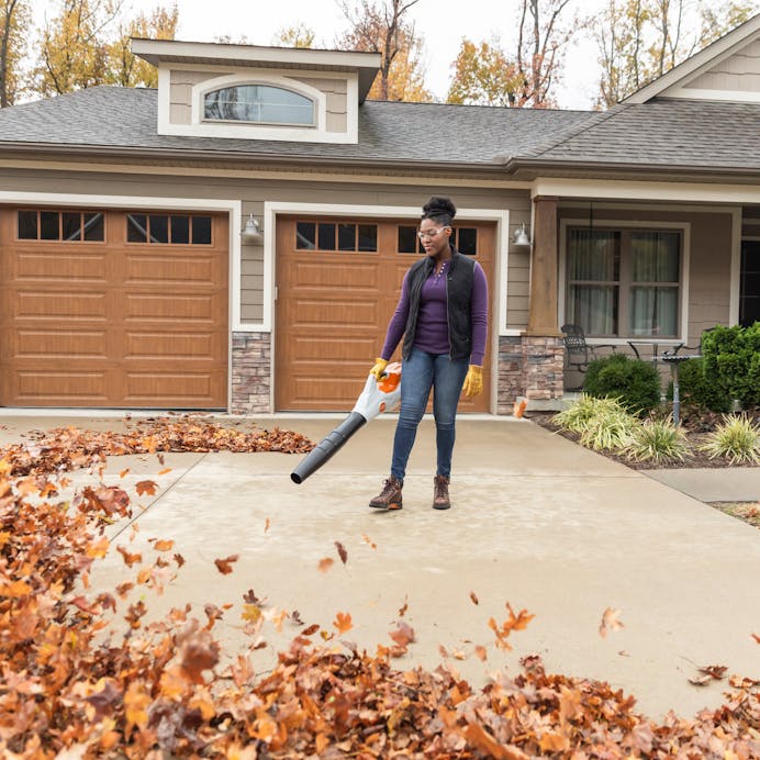 Woman blowing leaves off of her driveway with a Stihl Cordless Blower